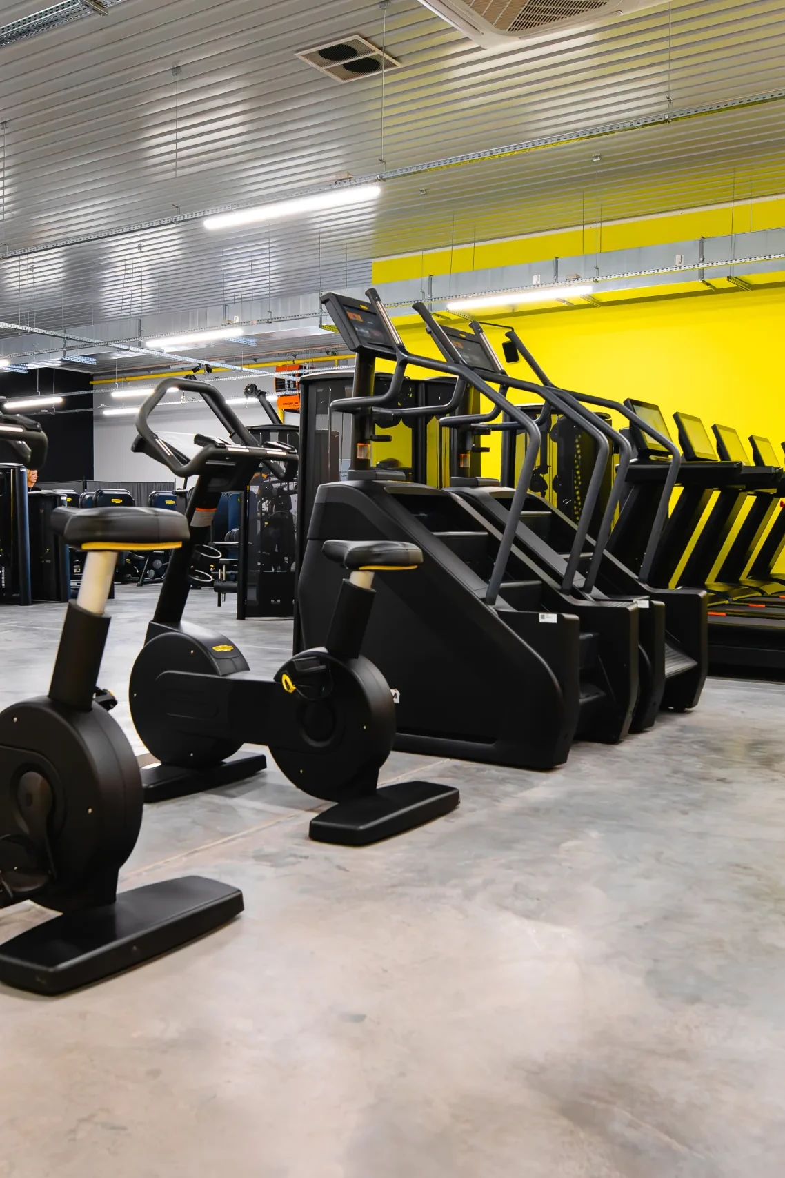 Rowery stacjonarne, stepper schodowy i bieżnie przy żółtej ścianie w strefie cardio – siłownia Funfit II Bohaterów Getta 9 w Nowej Soli