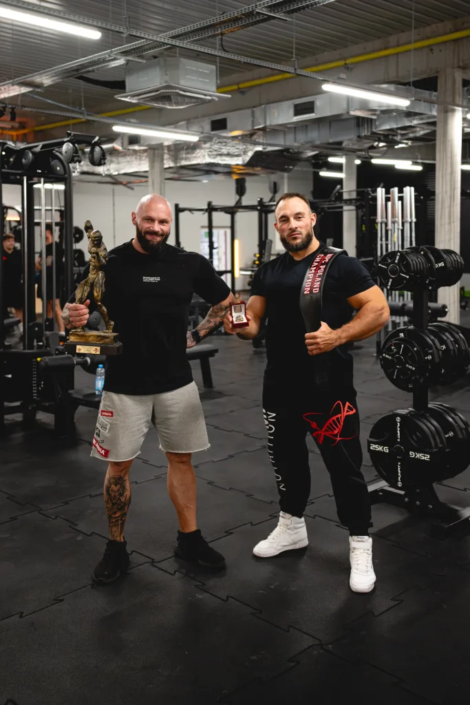 Łukasz Mizera i Szymon Dziubek, trenerzy Funfit II, z trofeami kulturystycznymi na sali siłowej klubu w Nowej Soli